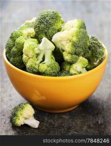Bunch of fresh green broccoli in yellow bowl over wooden background - healthy or vegetarian food concept