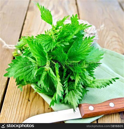 Bunch of fresh green nettle, a knife, a skein of twine on a napkin on a wooden boards background