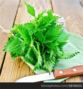 Bunch of fresh green nettle, a knife, a skein of twine on a napkin on a wooden boards background