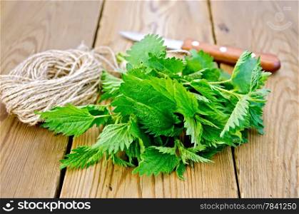 Bunch of fresh green nettle, knife, ball of twine on a wooden boards background