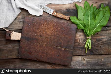 bunch of fresh green sorrel leaves and old brown cutting board on a wooden table, top view