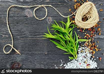 Bunch of fresh green tarragon with salt, pepper, fenugreek seeds and a coil of twine against a black wooden board
