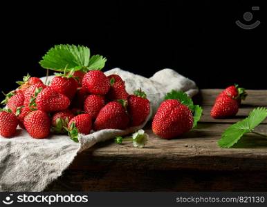 bunch of fresh ripe red strawberries on a gray linen napkin, wooden table, black background