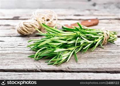 Bunch of fresh rosemary tied with twine, skein of rope and a knife on wooden board background