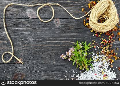 Bunch of fresh thyme with green leaves and pink flowers, salt, pepper, fenugreek seeds and a coil of twine against a black wooden board