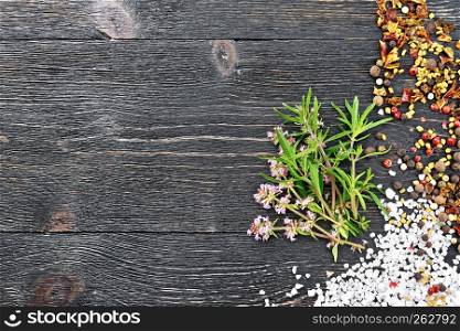 Bunch of fresh thyme with green leaves and pink flowers with salt, pepper, fenugreek seeds on a black wooden board background