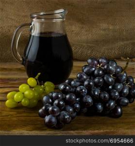 Bunch of grapes and a Wine jug on a dark wooden background. Bunch of grapes. Cluster grapes. Bunch grapes. Grapes. Grape. Glass of wine. Glass wine. Grape vine