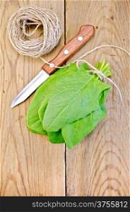 Bunch of green spinach, knife, twine on the background of wooden boards