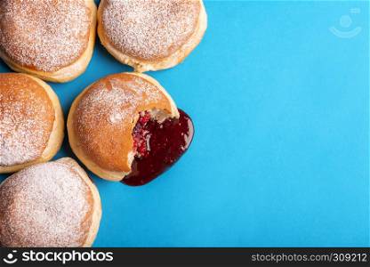 Bunch of jam doughnuts, filled with strawberry jelly, covered with powdered sugar, on a blue paper background. Flat lay with sweet food.