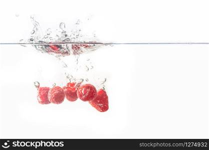 Bunch of juicy delicious looking raspberries splashing into water surface and sinking. Isolated on white background, splash food photography.. Bunch of raspberries splashing into water surface and sinking. Isolated on white background.