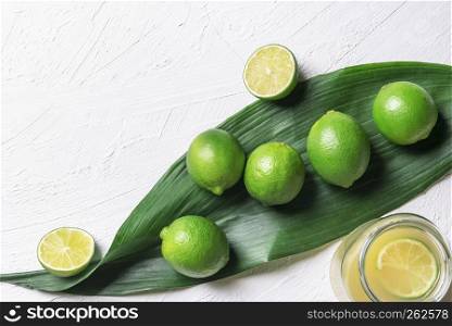 Bunch of limes on a big green leaf and a jar with freshly squeezed lime juice, on a white background. Above view with copy space. Detox context.