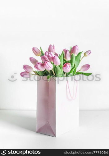 Bunch of pink blooming tulips in gift box on table at white wall background. Celebrating in mothers day in springtime with beautiful flowers. Front view.