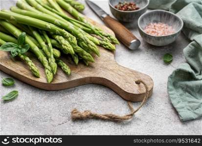 Bunch of raw asparagus stems with different spices on grey concrete background