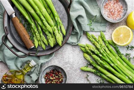 Bunch of raw asparagus stems with different spices on grey concrete background