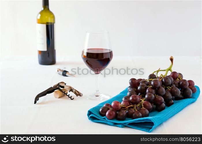 Bunch of red grapes and a glass of red wine with a wine bottle on a white tablecloth. Bunch of red grapes and a glass of red wine with a wine bottle