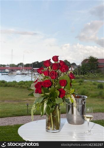 Bunch of red roses in vase on patio table with white wine in harbor setting