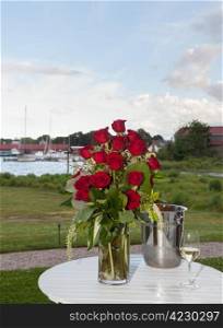 Bunch of red roses in vase on patio table with white wine in harbor setting