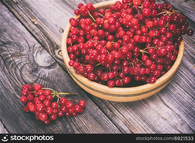 bunch of red viburnum in a wooden bowl on a gray table, top view