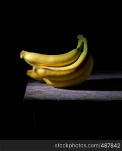 bunch of yellow unpeeled ripe bananas on a gray wooden table, black background