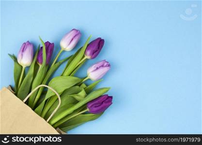 bunch purple tulips with brown paper bag arranged corner against blue background. High resolution photo. bunch purple tulips with brown paper bag arranged corner against blue background. High quality photo