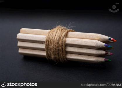 Bundle of colored pencils wrapped with string on black