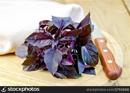 Bundle of purple basil, napkin, knife on background wooden plank