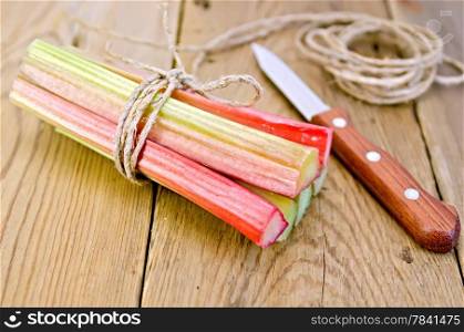 Bundle of stalks of rhubarb, a knife and a coil of rope on the background of wooden boards