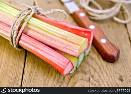 Bundle of stalks of rhubarb with a knife and a coil of rope on the background of wooden boards