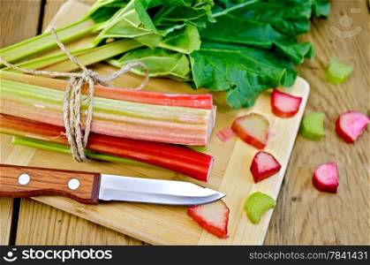 Bundle of stalks rhubarb, rhubarb pieces with a sheet and a knife on a wooden board