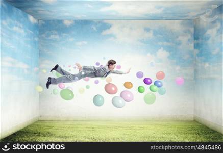 Buoyant and happy. Young man flying in sky among colorful balloons