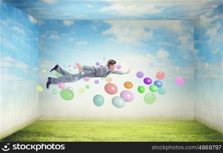 Buoyant and happy. Young man flying in sky among colorful balloons