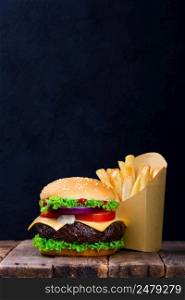 Burger and fries menu on wooden table with blank black chalkboard on background with copy space