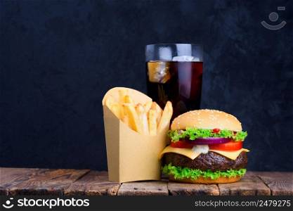 Burger fries and glass of soft cold drink with ice on wooden table with blank black chalkboard on background