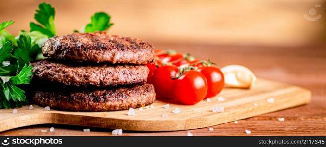 Burger grill on a cutting board with greens and tomatoes. On a wooden background. High quality photo. Burger grill on a cutting board with greens and tomatoes.
