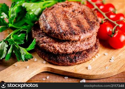 Burger grill on a cutting board with greens and tomatoes. On a wooden background. High quality photo. Burger grill on a cutting board with greens and tomatoes.