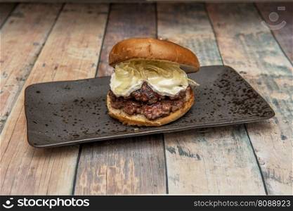 Burger with double beef, double goat cheese and caramelized onion on a black tray