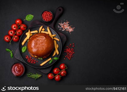 Burger with juicy beef cutlet, cheese, tomatoes, salt, spices and herbs on a dark concrete background