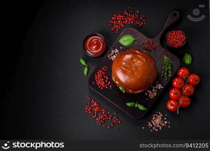 Burger with juicy beef cutlet, cheese, tomatoes, salt, spices and herbs on a dark concrete background