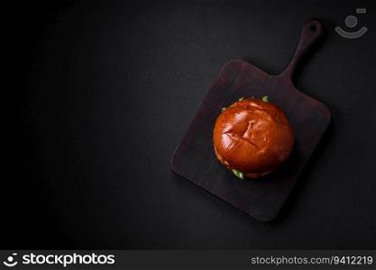Burger with juicy beef cutlet, cheese, tomatoes, salt, spices and herbs on a dark concrete background