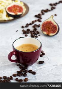 Burgundy cup with freshly brewed espresso on a gray background. Roasted coffee beans are located around a cup of coffee. In the background is fresh figs and homemade cheese.. Burgundy cup with freshly brewed espresso on a gray background. Roasted coffee beans are located around a cup of coffee. In the background is fresh figs and homemade cheese. Close-up.