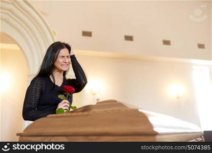 burial, people and mourning concept - crying unhappy woman with red rose and coffin at funeral in church. crying woman with red rose and coffin at funeral