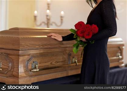 burial, people and mourning concept - unhappy woman with red roses and coffin at funeral in church. sad woman with red roses and coffin at funeral