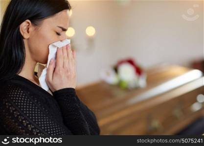 burial, people, grief and mourning concept - close up of sad woman with paper wipe crying near coffin at funeral in church. woman crying near coffin at funeral in church