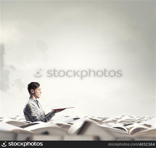Buried in knowledge and studying. Young man sitting in pile of old books