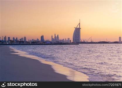 Burj Al Arab in Jumeirah Island or boat building with waves on sea beach, Dubai Downtown skyline, United Arab Emirates or UAE. Financial district in urban city. Skyscrapers at sunset.