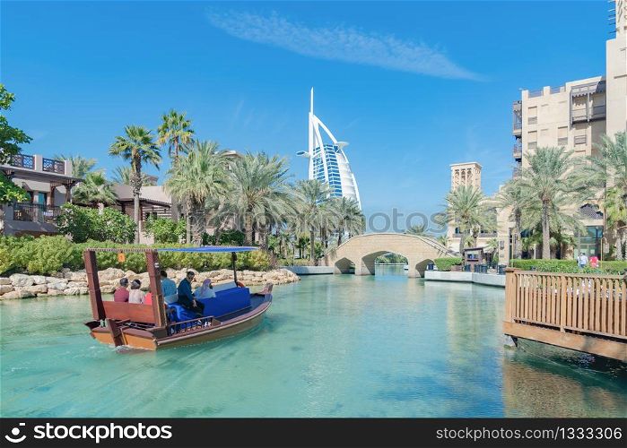 Burj Al Arab Jumeirah Island or boat building with turquoise lake or river and reflection, Dubai Downtown skyline, United Arab Emirates or UAE. Hotel in urban city at noon in travel vacation concept.