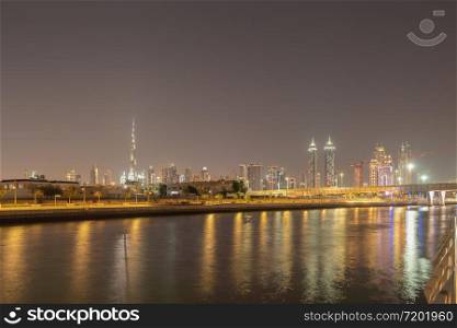 Burj Khalifa with lake or river and bridge in Dubai Downtown skyline, United Arab Emirates or UAE. Financial district and business area in urban city. Skyscraper buildings at night. Reflection.