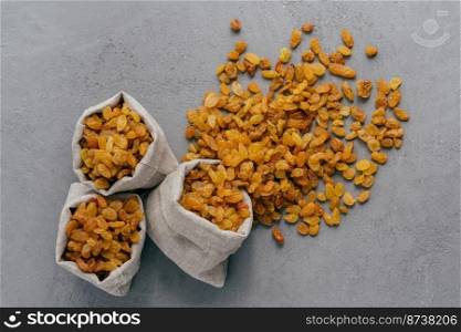 Burlap sacks with dry raisins spilled out over grey texture background. View from above. Dried fruit. Healthy nutrition concept