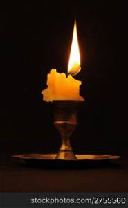 Burning candle. An ancient candlestick, a dark background