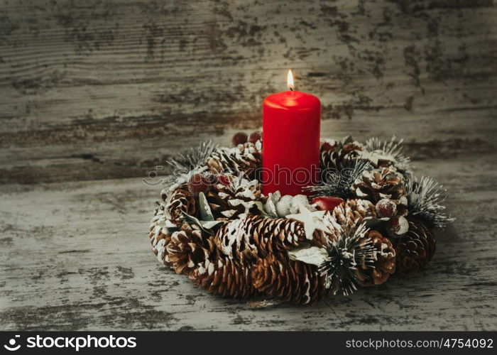 Burning candle in a Christmas wreath with seasonal decorations.